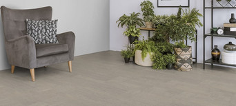 Der Boden im Wohnzimmer ist mit hellgrauem Kork belegt. Es gibt einen bequemen Sessel und einen Ständer mit Grünpflanzen.